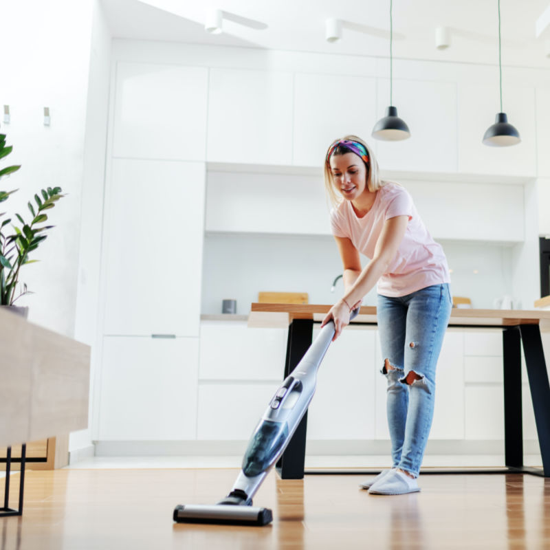 woman cleaning linoleum floor with an electric steam mop and white cabinetry