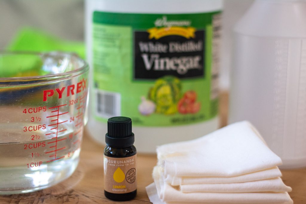 lemon essential oil and vinegar on a table with a measuring cup and cloth rags